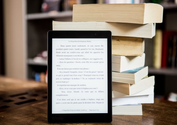 Une liseuse allumée avec une pile de livres derrière