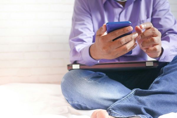 Photographie d'une personne utilisant un smarphone tout en ayant un ordinateur portable posé sur les genoux.